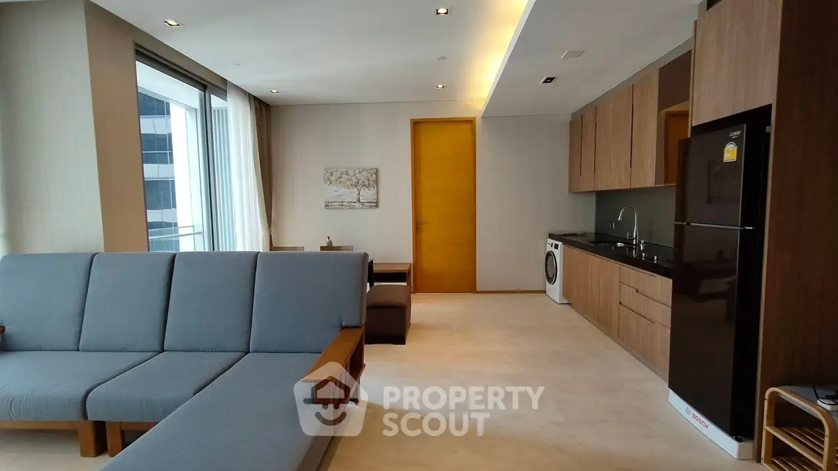 Modern living room with sleek kitchen, featuring a washing machine and stylish furniture.
