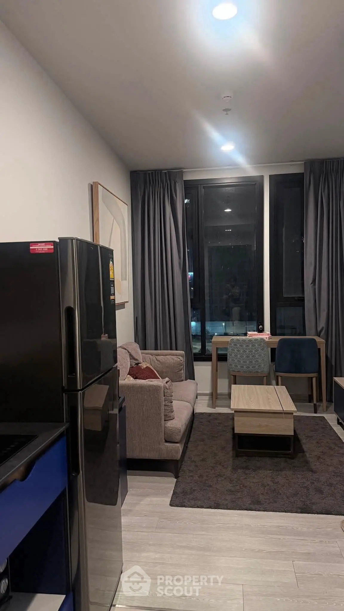 Modern living room with cozy seating and sleek refrigerator in stylish apartment.