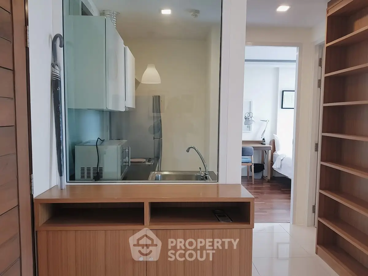 Modern apartment interior with kitchenette and view into bedroom, featuring sleek cabinetry and contemporary design.