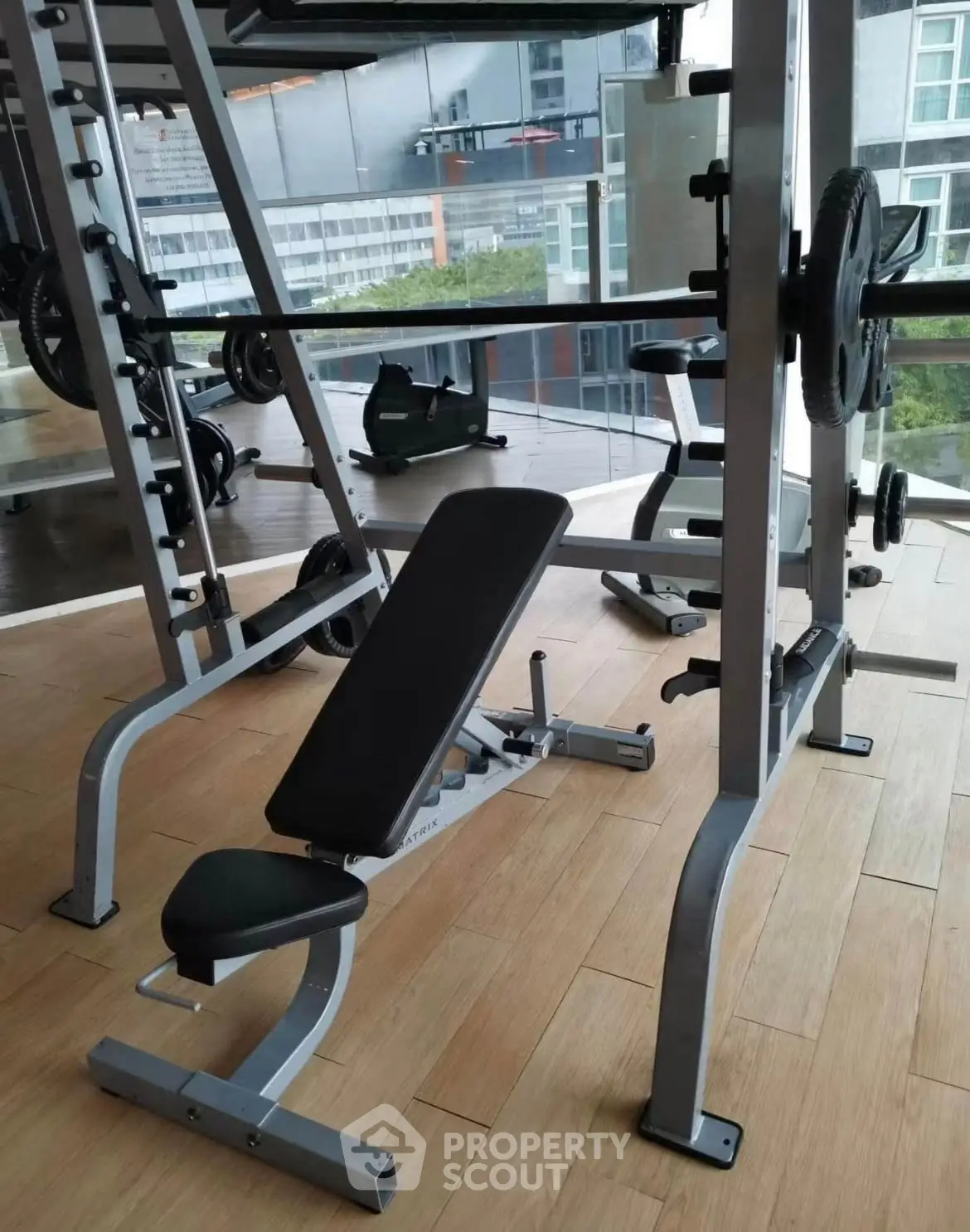 Modern gym with weightlifting equipment and city view, perfect for fitness enthusiasts.