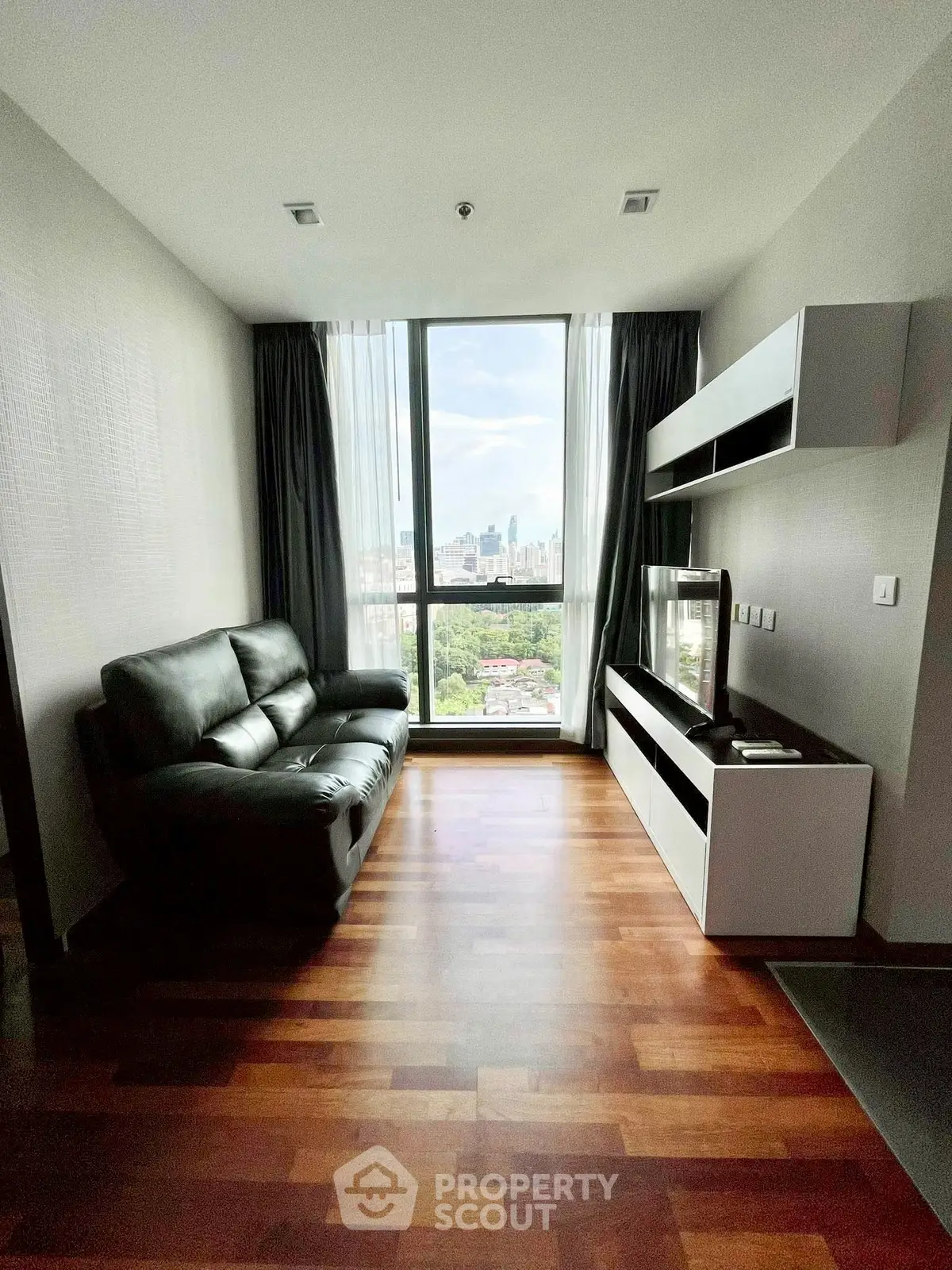 Modern living room with city view, featuring sleek furniture and large windows.