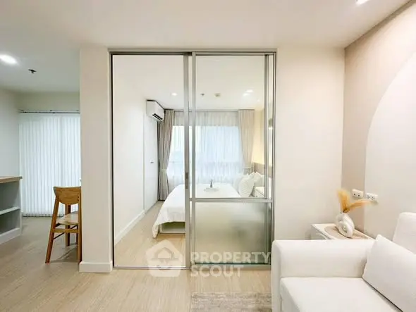 Modern open-plan living room with sliding glass doors leading to a cozy bedroom, featuring elegant decor and natural light.