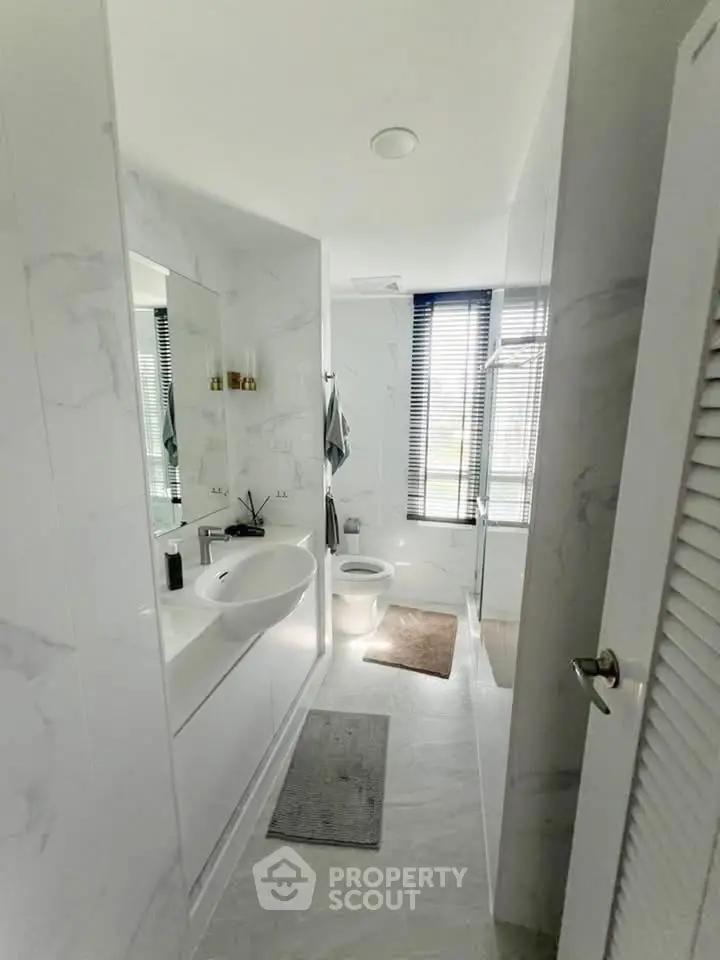 Modern bathroom with sleek design, featuring a large mirror, stylish sink, and natural light from window.