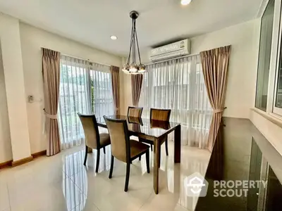 Spacious dining area with polished floor tiles, elegant chandelier, and large windows draped with stylish curtains, perfect for family gatherings.