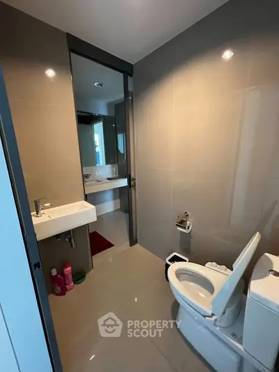Modern bathroom with sleek fixtures and neutral tiles, featuring a toilet and sink.