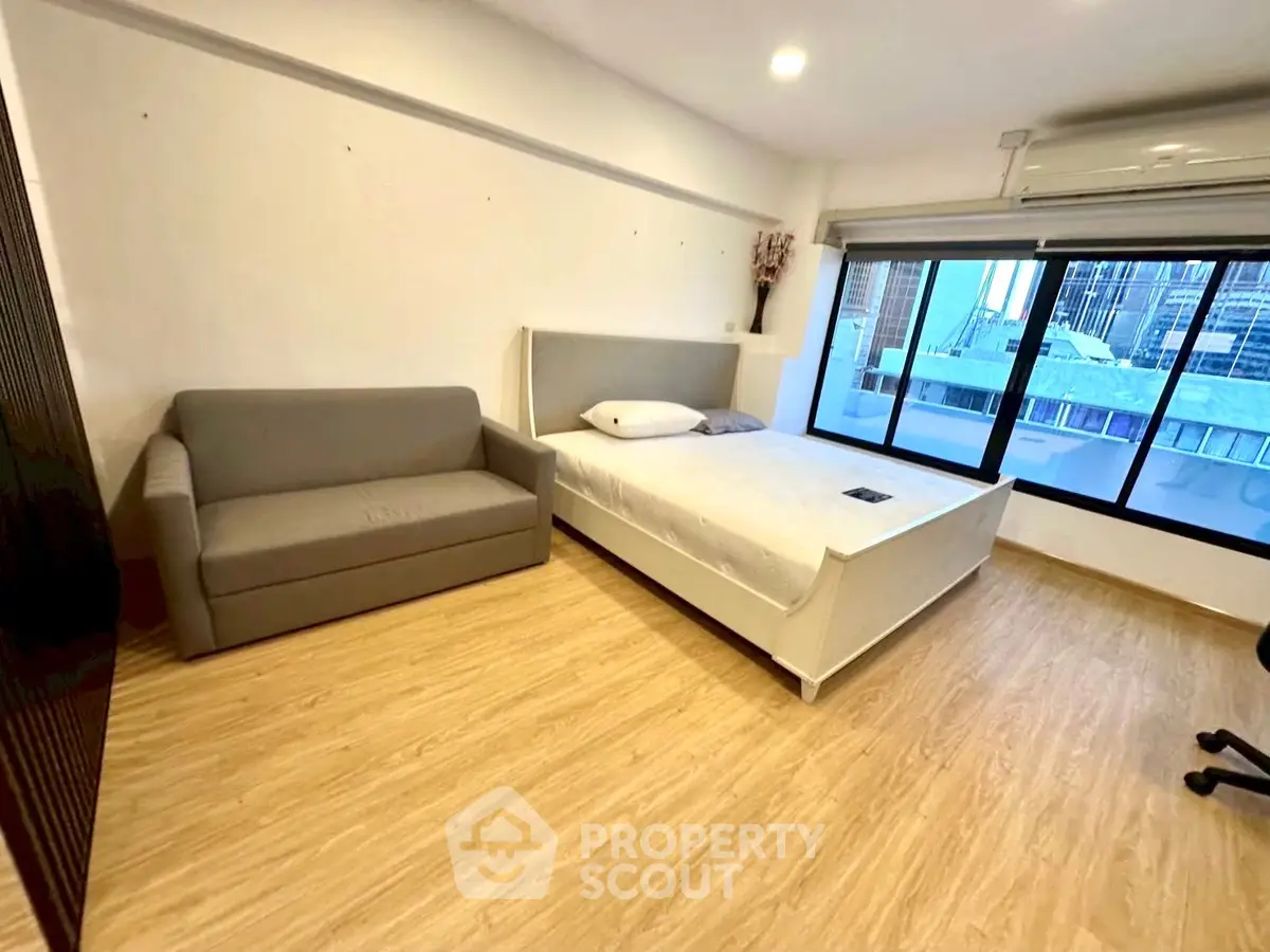 Spacious bedroom with large window and modern furnishings in urban apartment