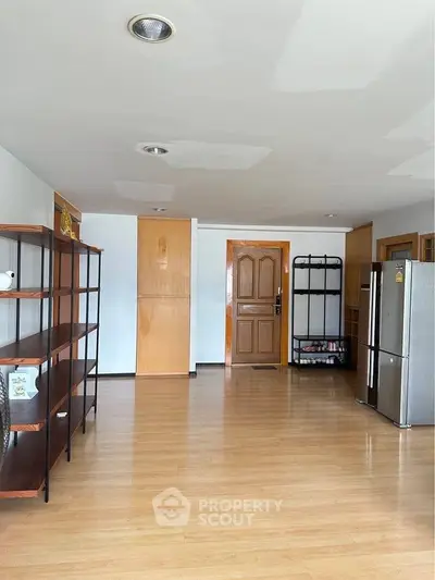 Spacious living area with wooden flooring and modern shelving units, featuring a sleek refrigerator.