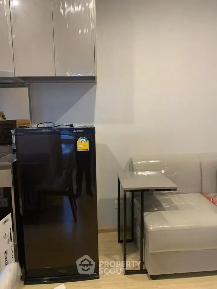 Modern apartment interior with compact kitchen and cozy living area featuring a sleek black fridge and stylish sofa.