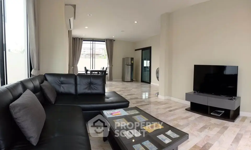 Spacious modern living room with sleek black leather sofa and flat-screen TV