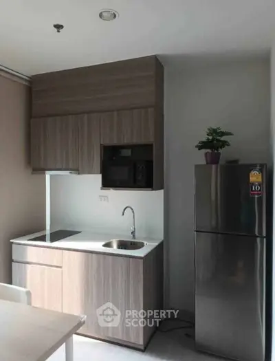 Modern compact kitchen with sleek cabinetry and stainless steel fridge in a cozy apartment.