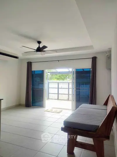 Spacious living room with large windows and modern ceiling fan, opening to a private garden area.