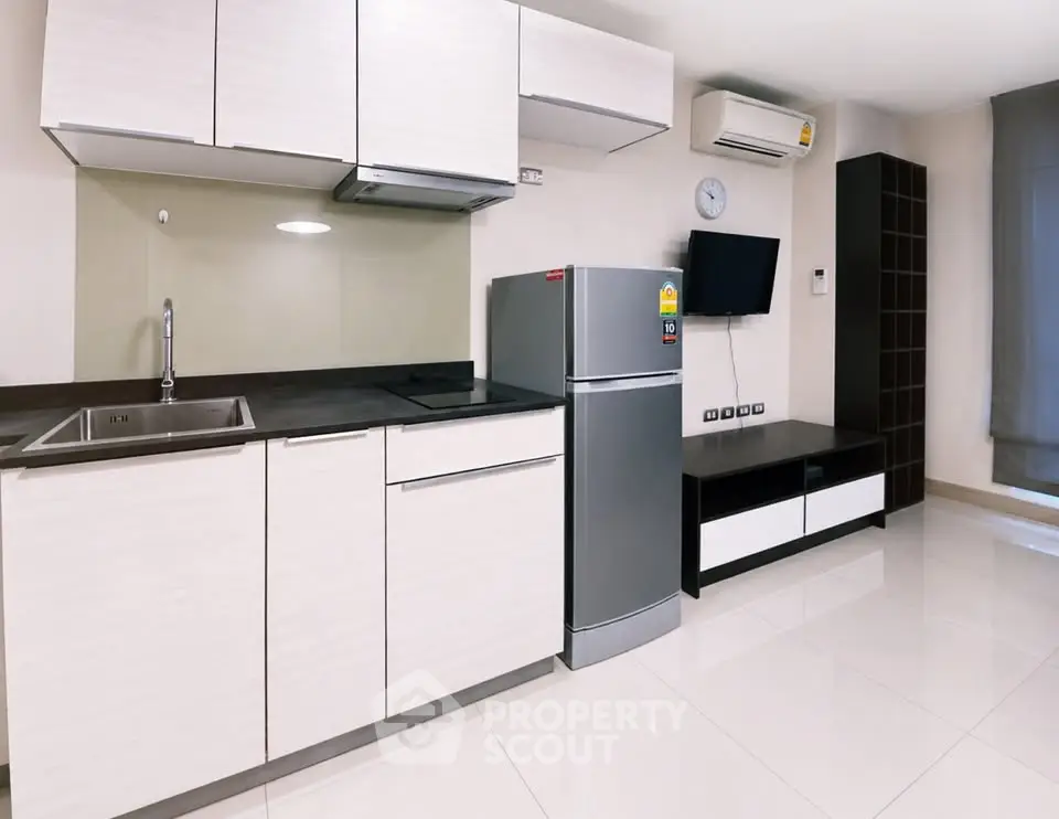Modern kitchen with sleek cabinets, stainless steel fridge, and wall-mounted TV in a stylish apartment.