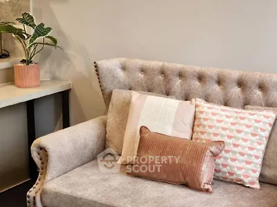 Elegant tufted sofa adorned with decorative pillows, complemented by a stylish plant and modern side table, perfect for a chic living space.