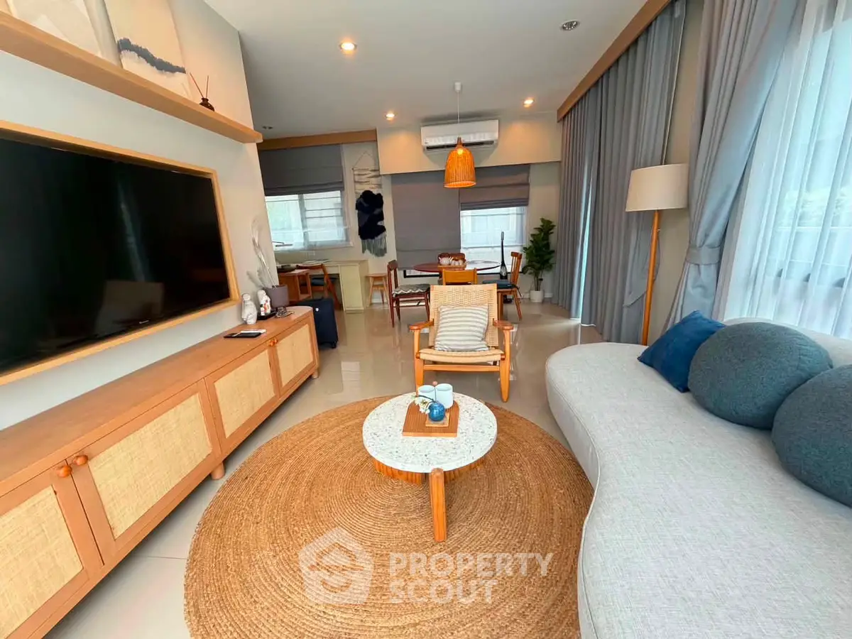 Modern living room with stylish furniture and large TV, featuring natural light and cozy decor.