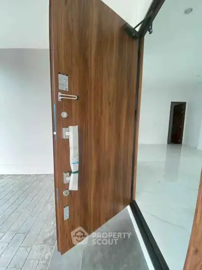 Modern wooden door opening to a spacious and bright interior with sleek flooring.
