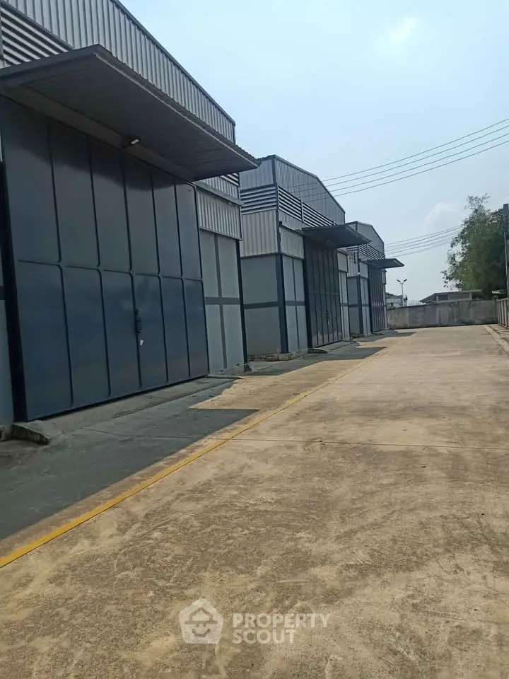 Modern industrial warehouse exterior with spacious driveway and secure fencing.