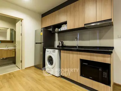 Modern kitchen with washing machine, fridge, and microwave in sleek apartment.