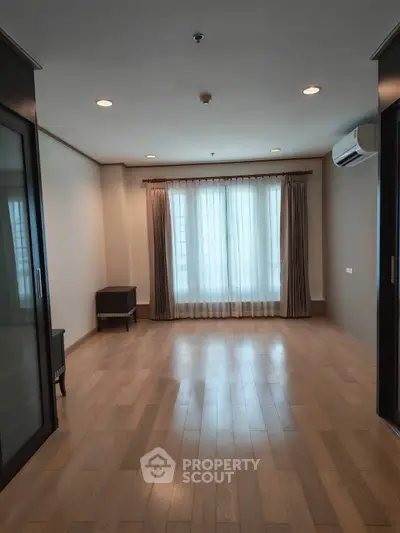 Spacious empty room with wooden flooring and large window, ideal for customization.