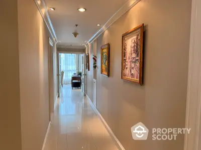 Elegant hallway with artwork leading to a bright room with large windows.