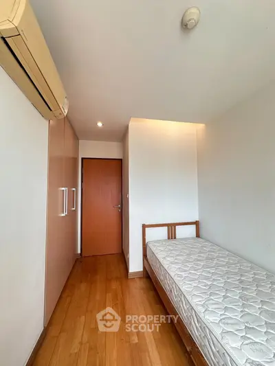 Cozy bedroom with wooden flooring, single bed, and built-in wardrobe in a modern apartment.