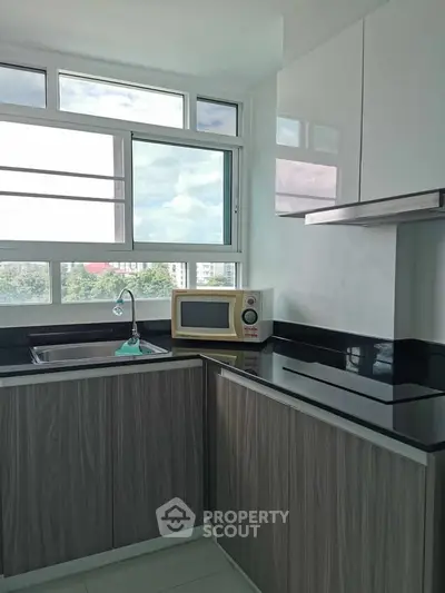 Modern kitchen with sleek cabinets and large window offering natural light and scenic view.