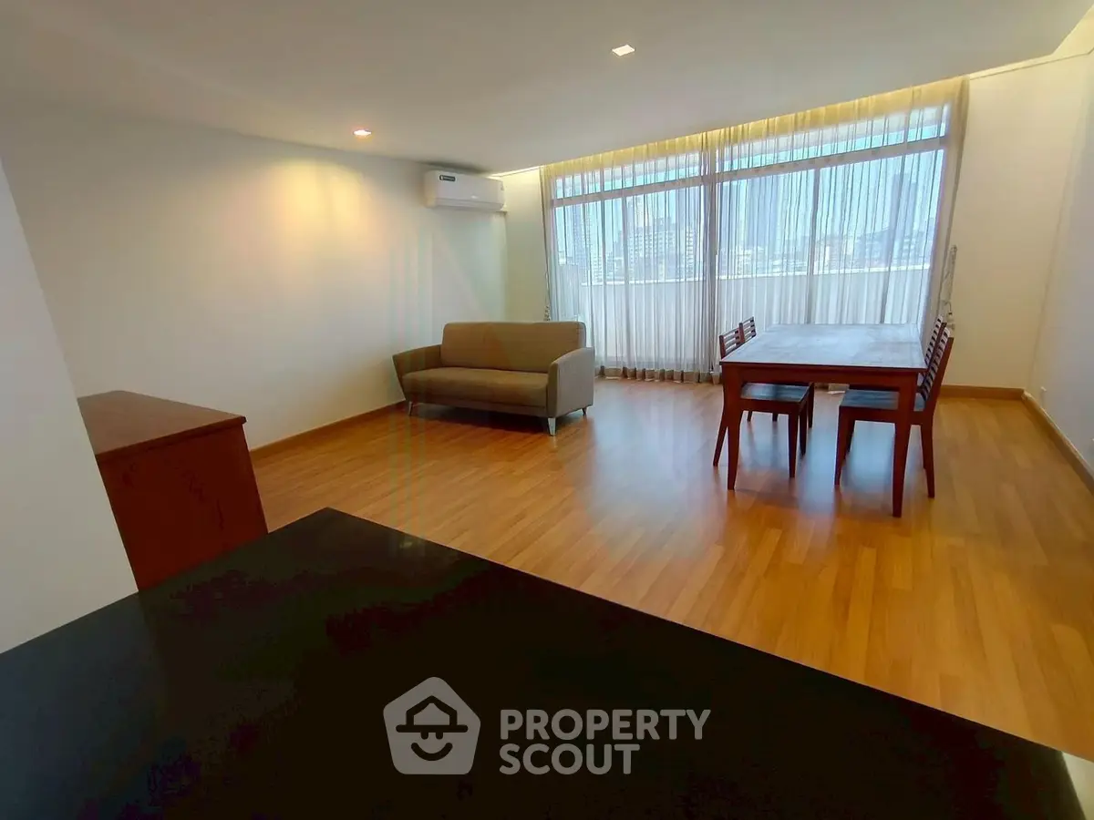 Spacious living room with wooden flooring and large windows offering natural light.
