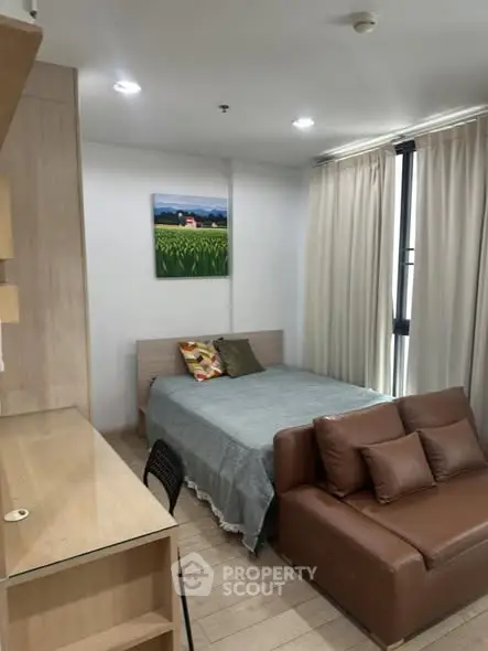 Cozy studio apartment with bed, sofa, and study desk, featuring natural light and modern decor.