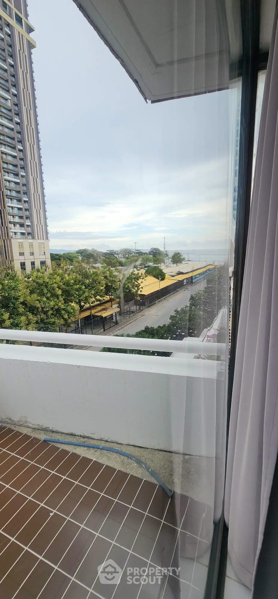 Stunning city view from a modern apartment balcony with glass railing and lush greenery.
