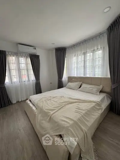 Spacious bedroom with large windows and elegant curtains, featuring a cozy bed and modern decor.
