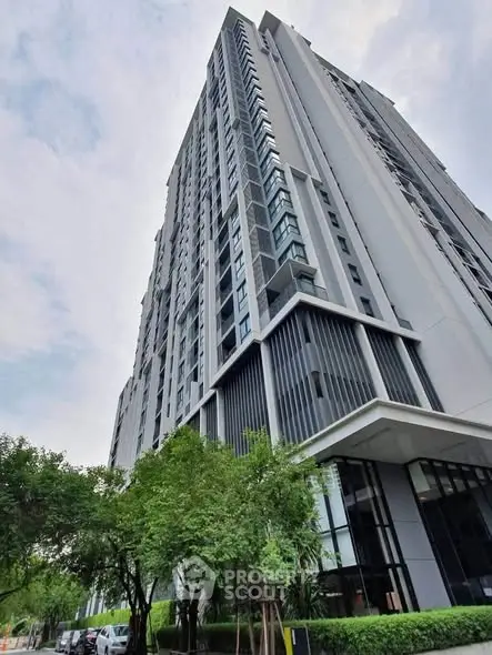 Modern high-rise building with sleek design and lush greenery at the base.
