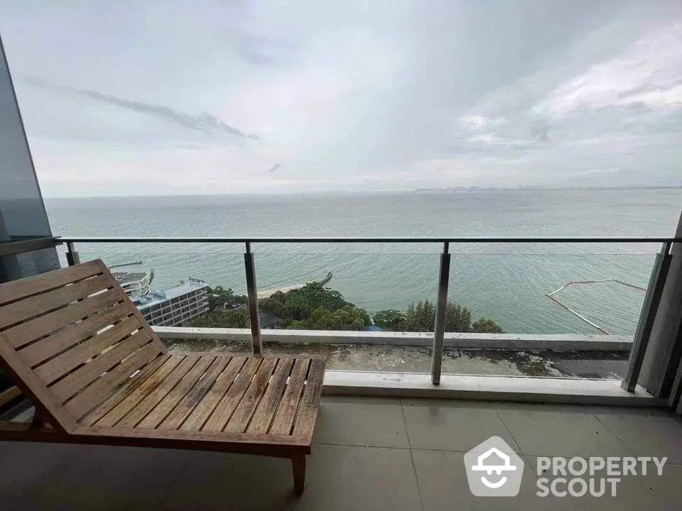 Stunning ocean view from a modern balcony with wooden lounge chair.