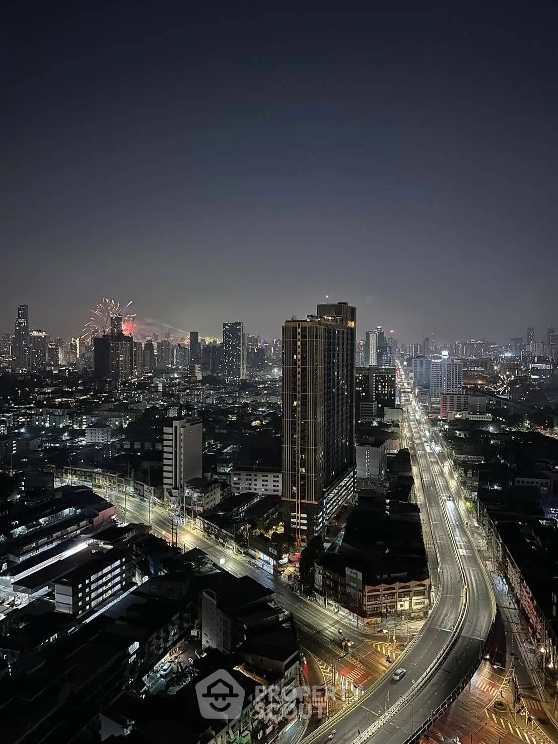 Stunning cityscape view from high-rise building at night with fireworks in the distance.