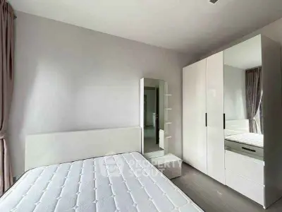 Modern minimalist bedroom with white furniture and ample natural light.