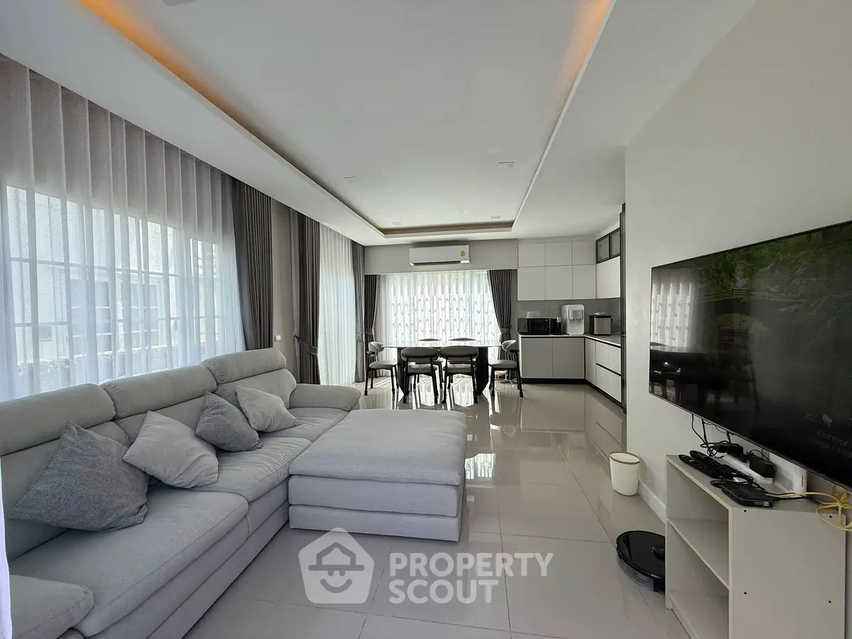 Spacious modern living room with open kitchen, sleek furniture, and abundant natural light.