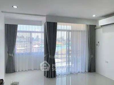 Bright living room with large windows and city view, featuring modern curtains and air conditioning.