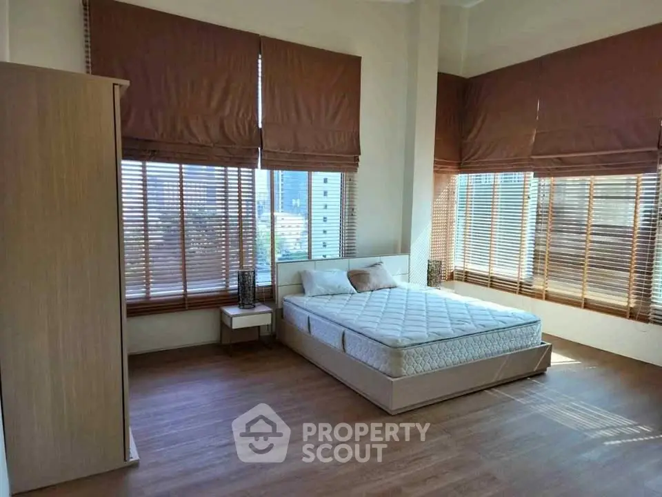 Spacious bedroom with large windows and wooden flooring, offering ample natural light and modern decor.
