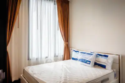 Cozy bedroom with large window and elegant curtains, featuring a comfortable bed and natural light.