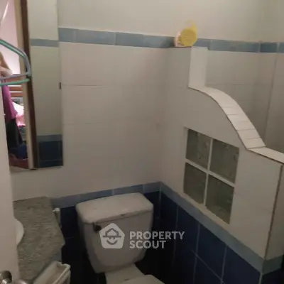 Compact bathroom with blue and white tiles, featuring a toilet and partial glass block wall.