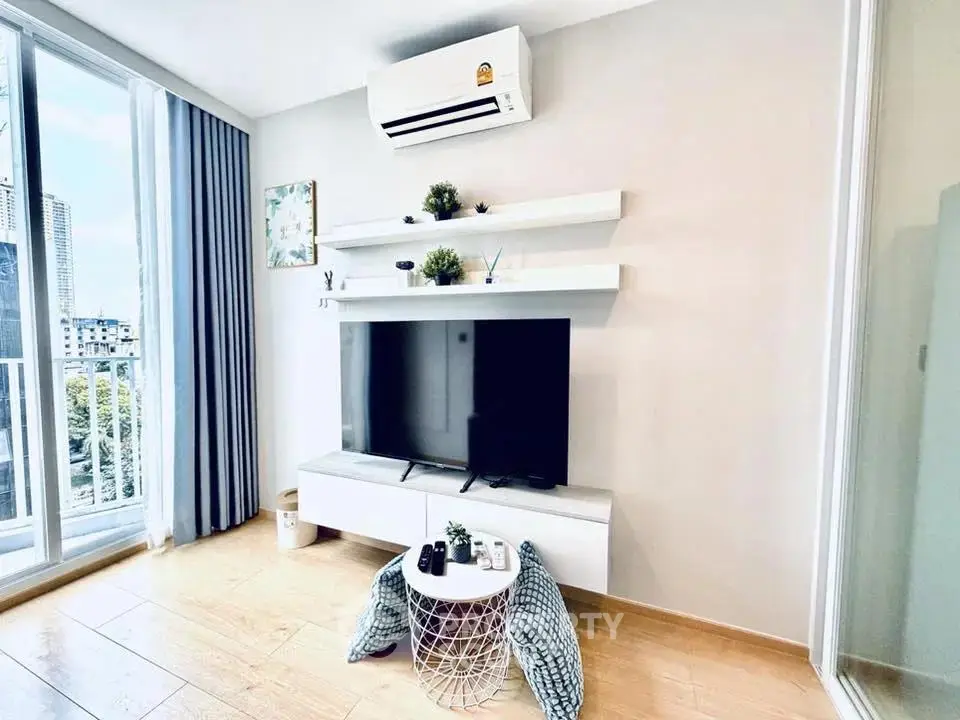 Modern living room with sleek TV setup and balcony view in urban apartment.