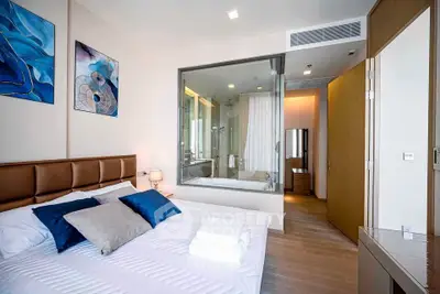 Modern bedroom with ensuite bathroom featuring glass partition and stylish decor.