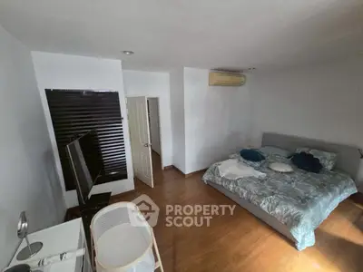 Spacious bedroom with modern decor and wooden flooring, featuring a cozy bed and air conditioning.