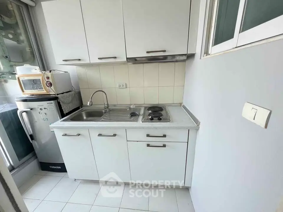 Compact kitchen with white cabinets and modern appliances in cozy apartment