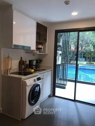 Modern kitchen with pool view, featuring washing machine and sleek cabinetry.