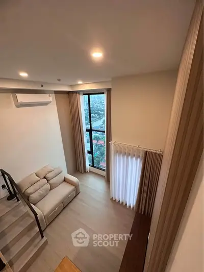 Modern loft-style living room with high ceiling and large window offering city views.