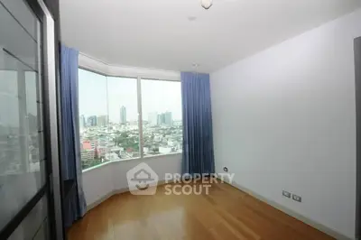 Spacious room with large window offering stunning city view and wooden flooring.