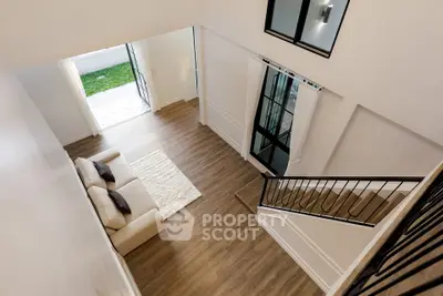 Spacious modern living room with high ceiling and elegant staircase, featuring large windows and stylish decor.