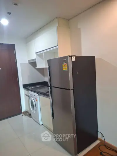 Modern kitchen with fridge, washing machine, and sleek cabinetry in compact layout.