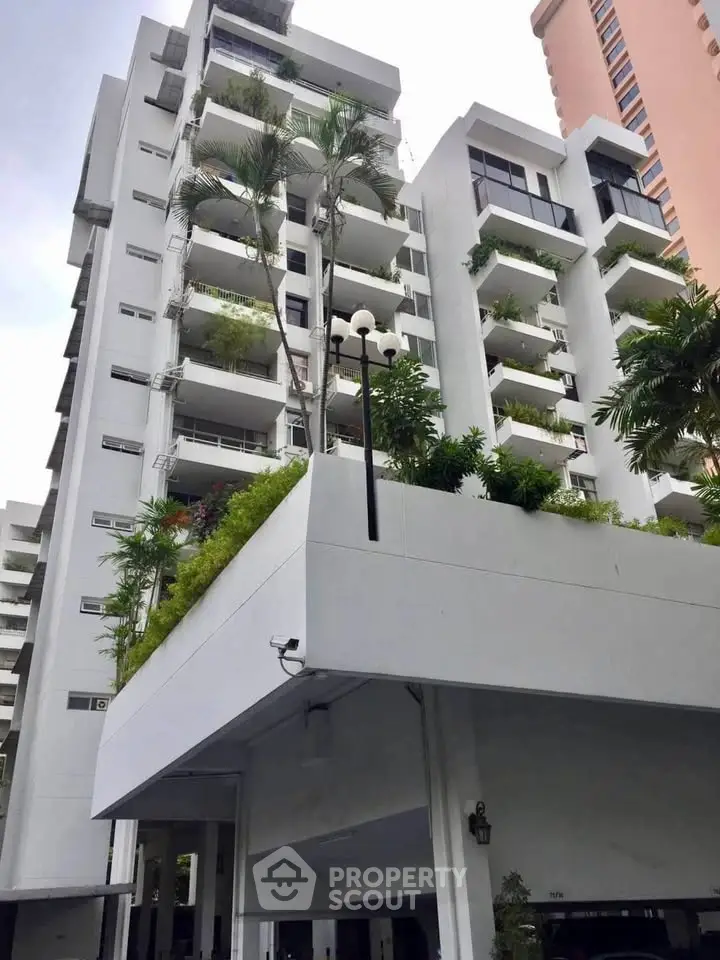 Modern high-rise building with lush greenery and spacious balconies in urban setting.