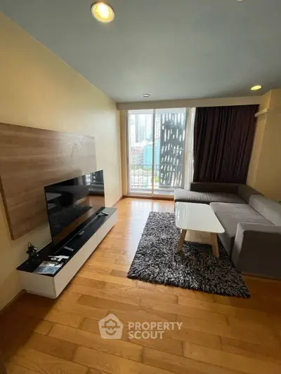 Modern living room with large TV, cozy sofa, and city view balcony.