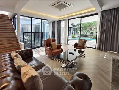 Luxurious living room with leather sofas and large windows overlooking a garden, featuring modern decor and natural light.